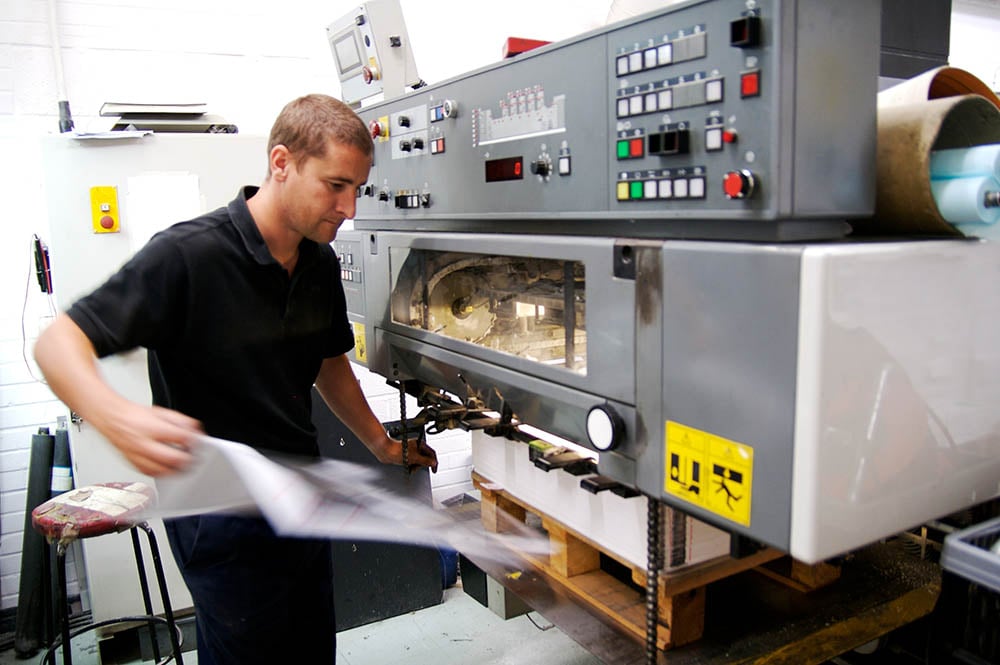 Pressman pulling sheet from printing press for inspection