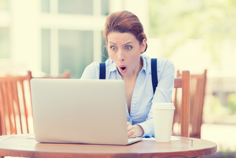 Shocked young business woman using laptop looking at computer screen blown away in stupor sitting outside corporate office. Human face expression, emotion, feeling, perception, body language, reaction